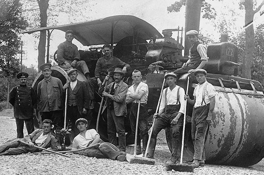 black and white photo of construction workers in front of a roller