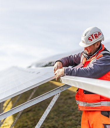 Foto eines STRABAG Bauarbeiters der dabei ist eine Photovoltaik-Anlage aufzubauen. 