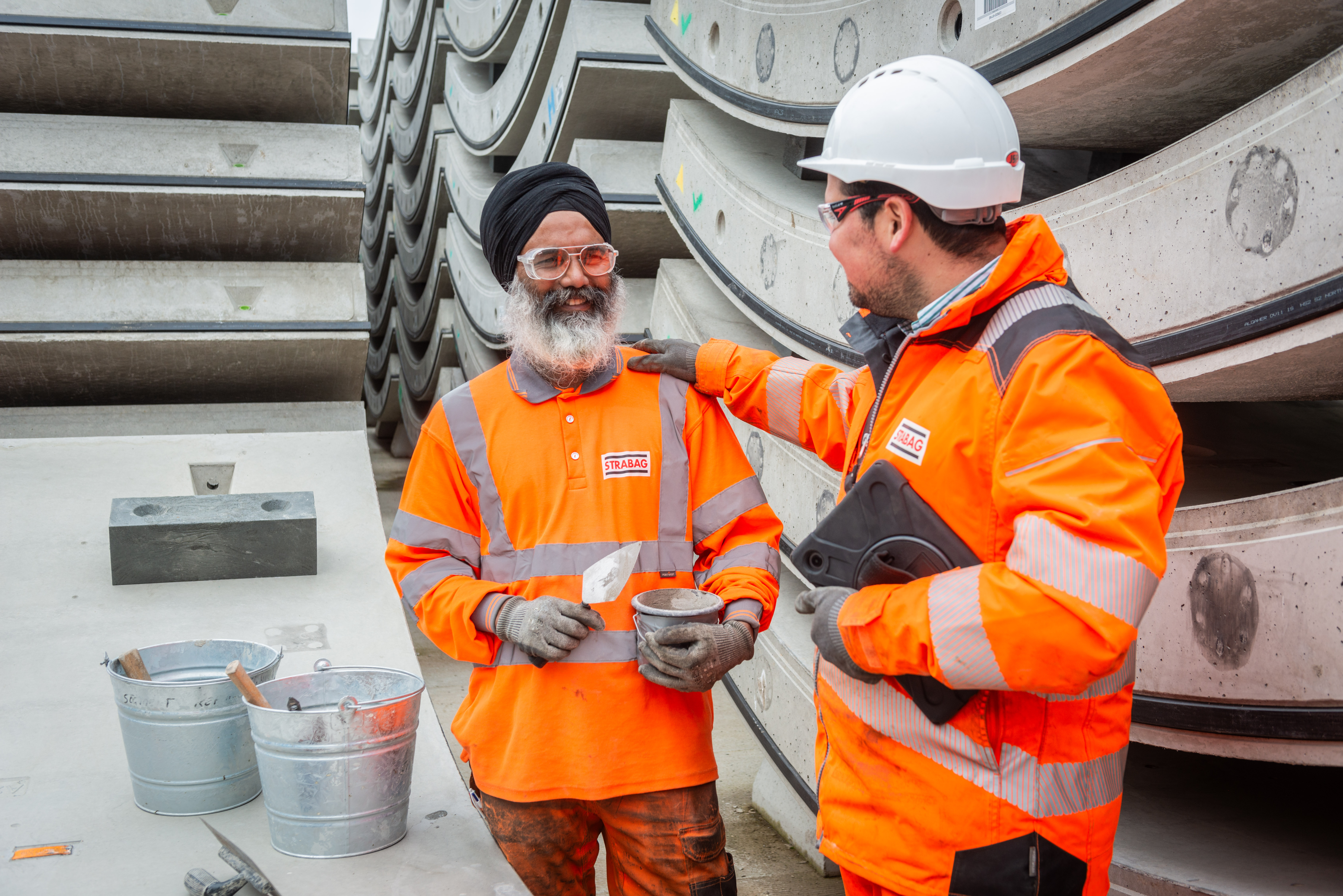 Photo of two construction colleagues chatting. One of the colleagues is wearing a special turban helmet