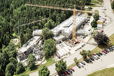 Photo shows an aerial view of a STRABAG construction site at the beginning of a wooded area. 