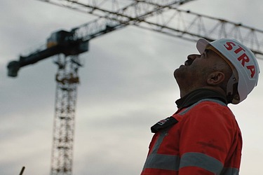 Foto eines Arbeiters mit STRABAG-Helm und Schutzkleidung, der nach oben blickt 