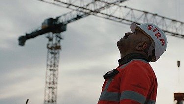 Photo of man looking at the sky, in the background you can see a crane