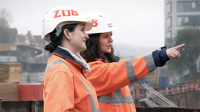 Foto von zwei Bauarbeiterinnen mit Zübin-Helmen die in die Ferne blicken