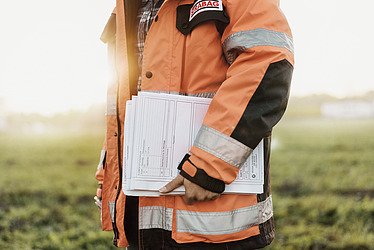 Foto zeigt eine Person in STRABAG-Kleidung und Dokumenten in der Hand die an einem Acker entlang geht